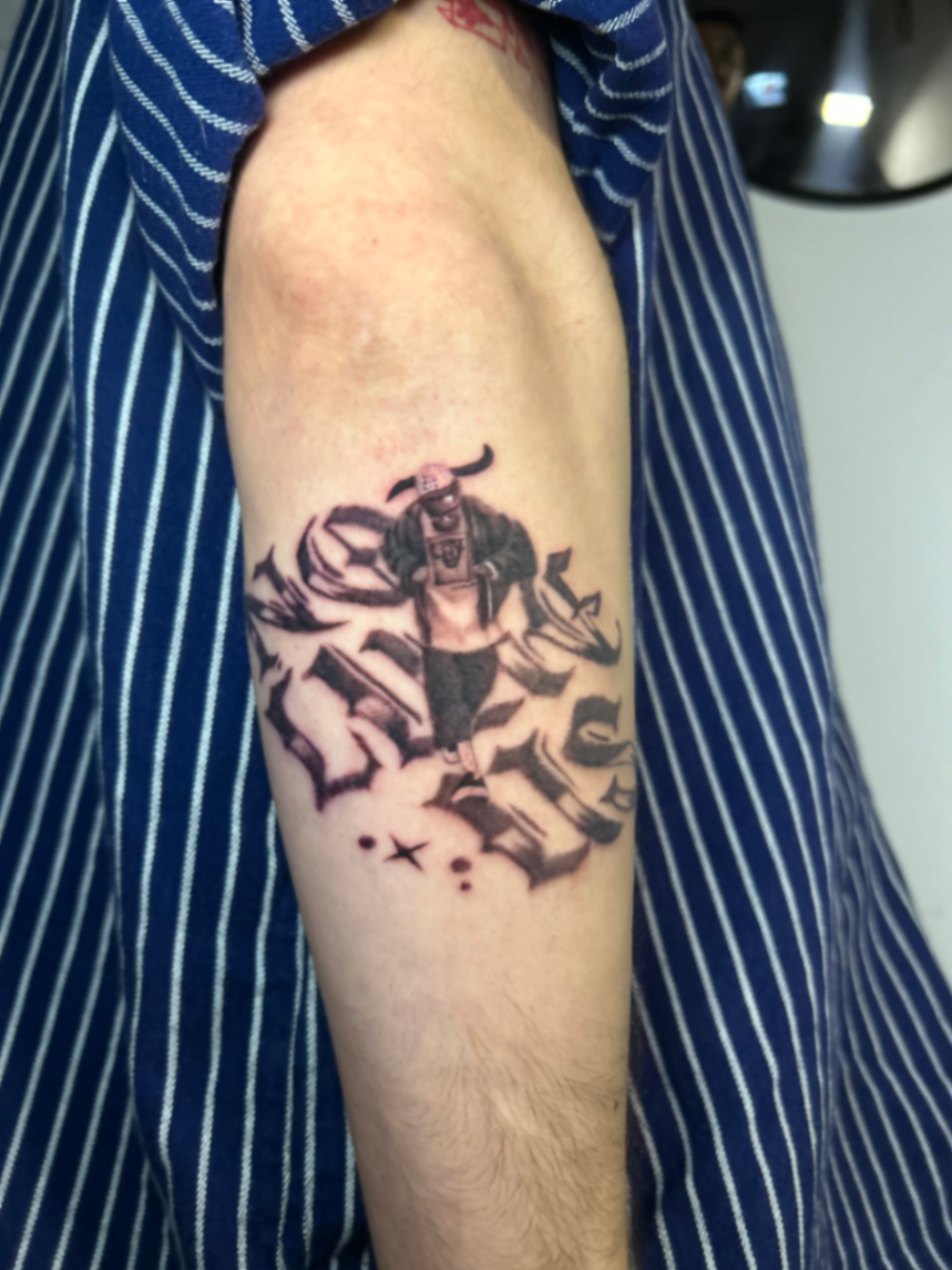 Black and grey lettering tattoo with a figure on the upper arm