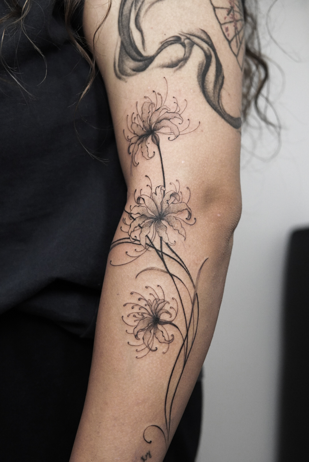 Black and grey spider lilies tattoo with flowing stems on the arm